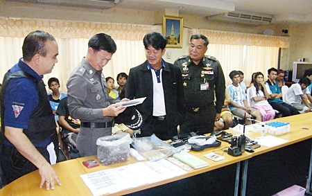 Chonburi Gov. Wichit Chatpaisit and high ranking police officials pour over the confiscated paraphernalia, as those arrested sit and wait processing behind them.